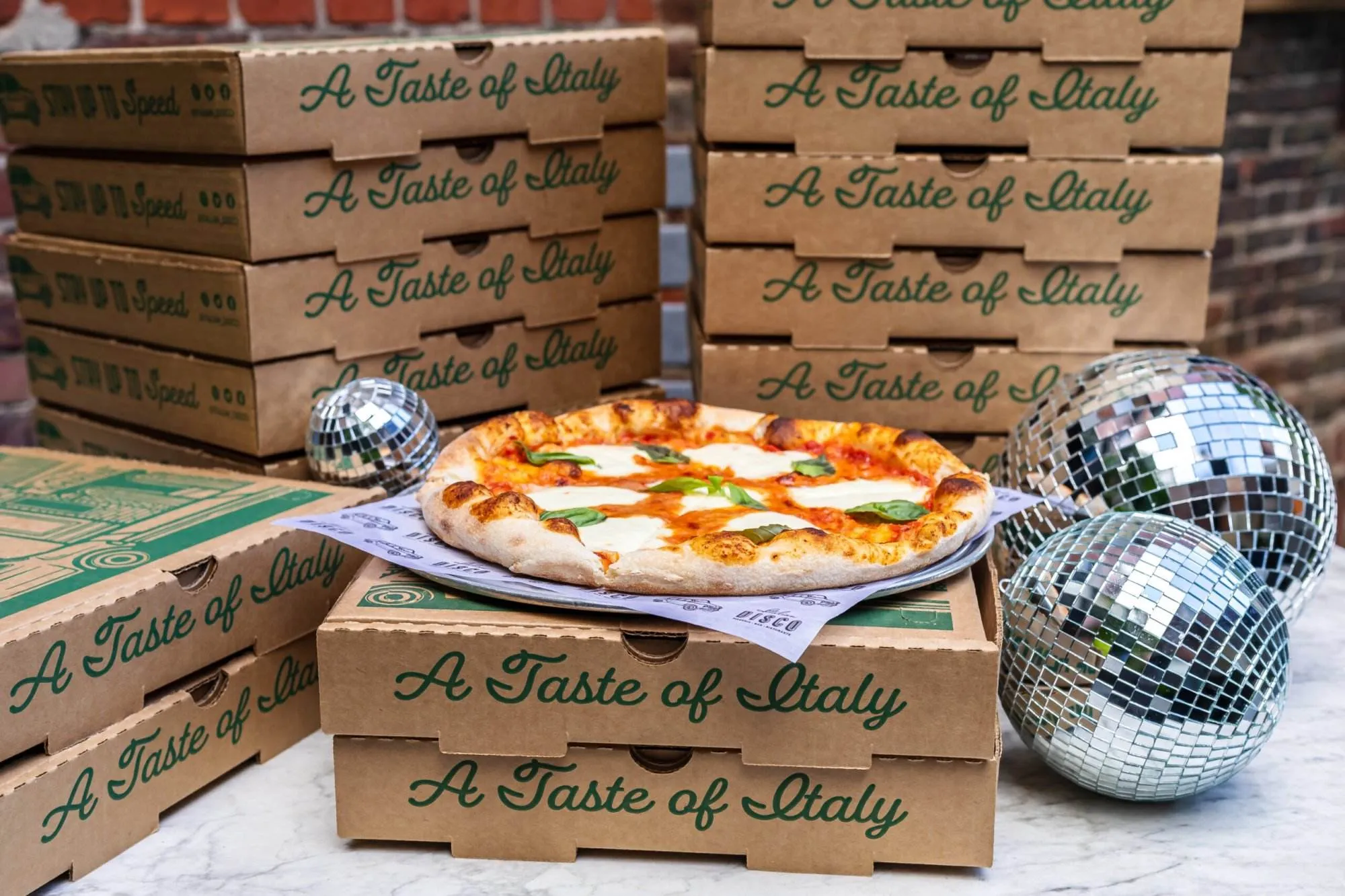 Image of stacks of pizza boxes with a pizza on top and disco balls to the right.